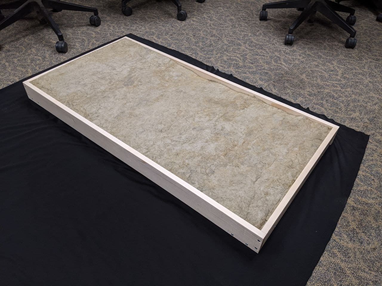 a panel with insulation inside on the ground about to be wrapped with black fabric